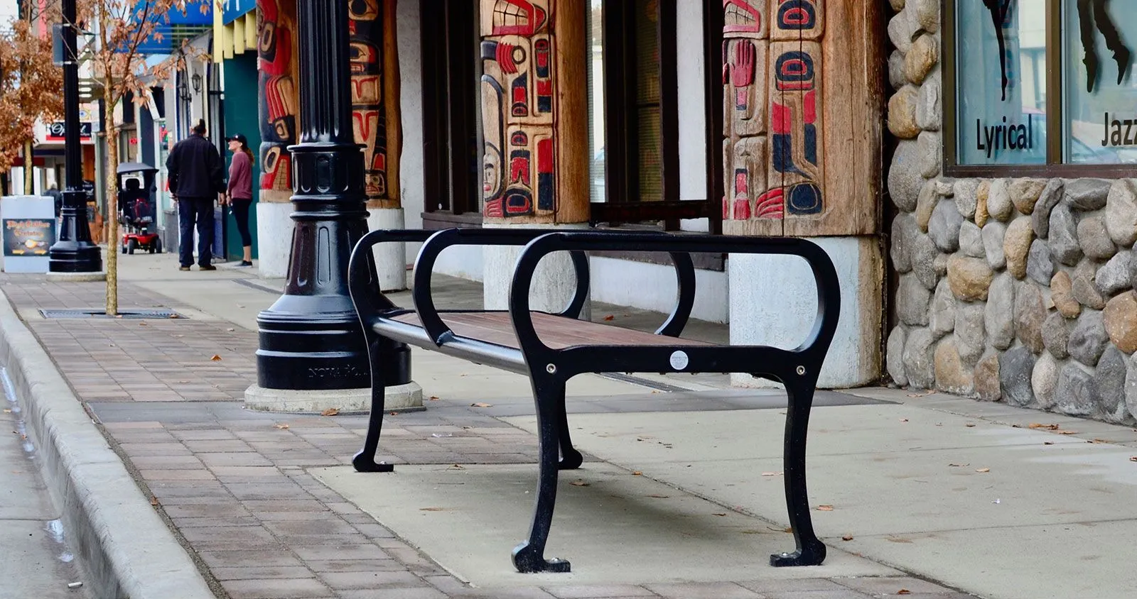 A Mountain Classic bench provides seating along a sidewalk in Mission, British Columbia. The bench features a black frame and wood-look recycled plastic lumber.