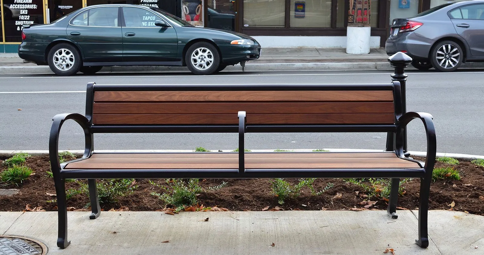 A Mountain Classic Wide Body Bench with center armrests provides comfortable seating along a city street. The bench features recycled plastic lumber and a durable powder-coated frame.