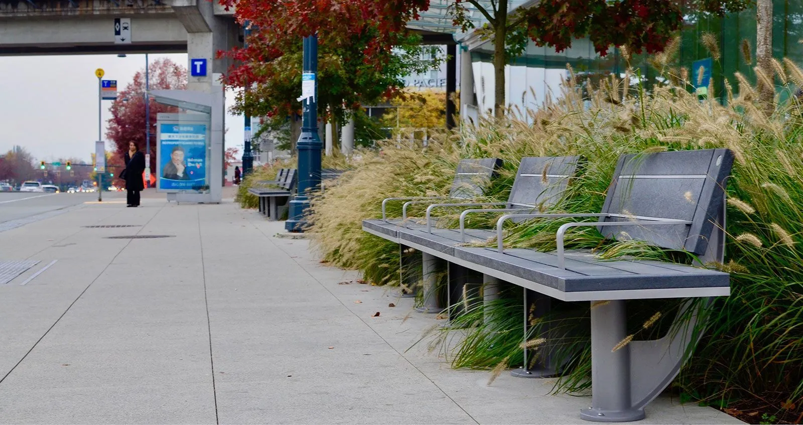 SurRe benches line a pedestrian walkway, complemented by ornamental grasses. These benches offer comfortable seating in a public space.
