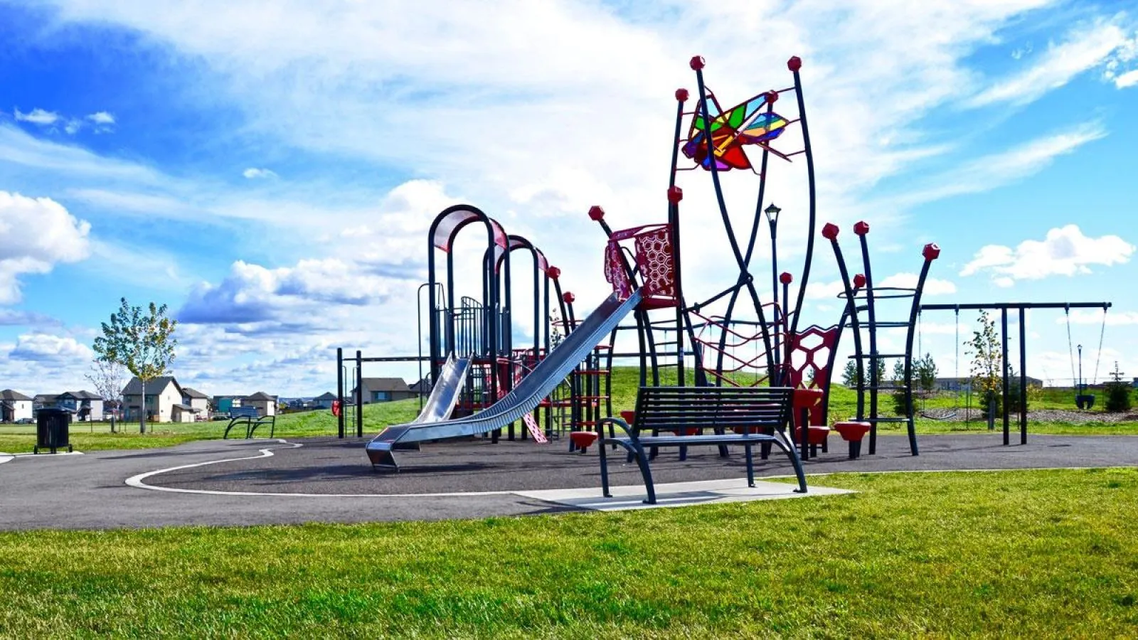 All-metal Modena park benches provide seating near a playground in the CY Becker Subdivision in Edmonton, Alberta. The benches offer a place to rest and enjoy the play area.