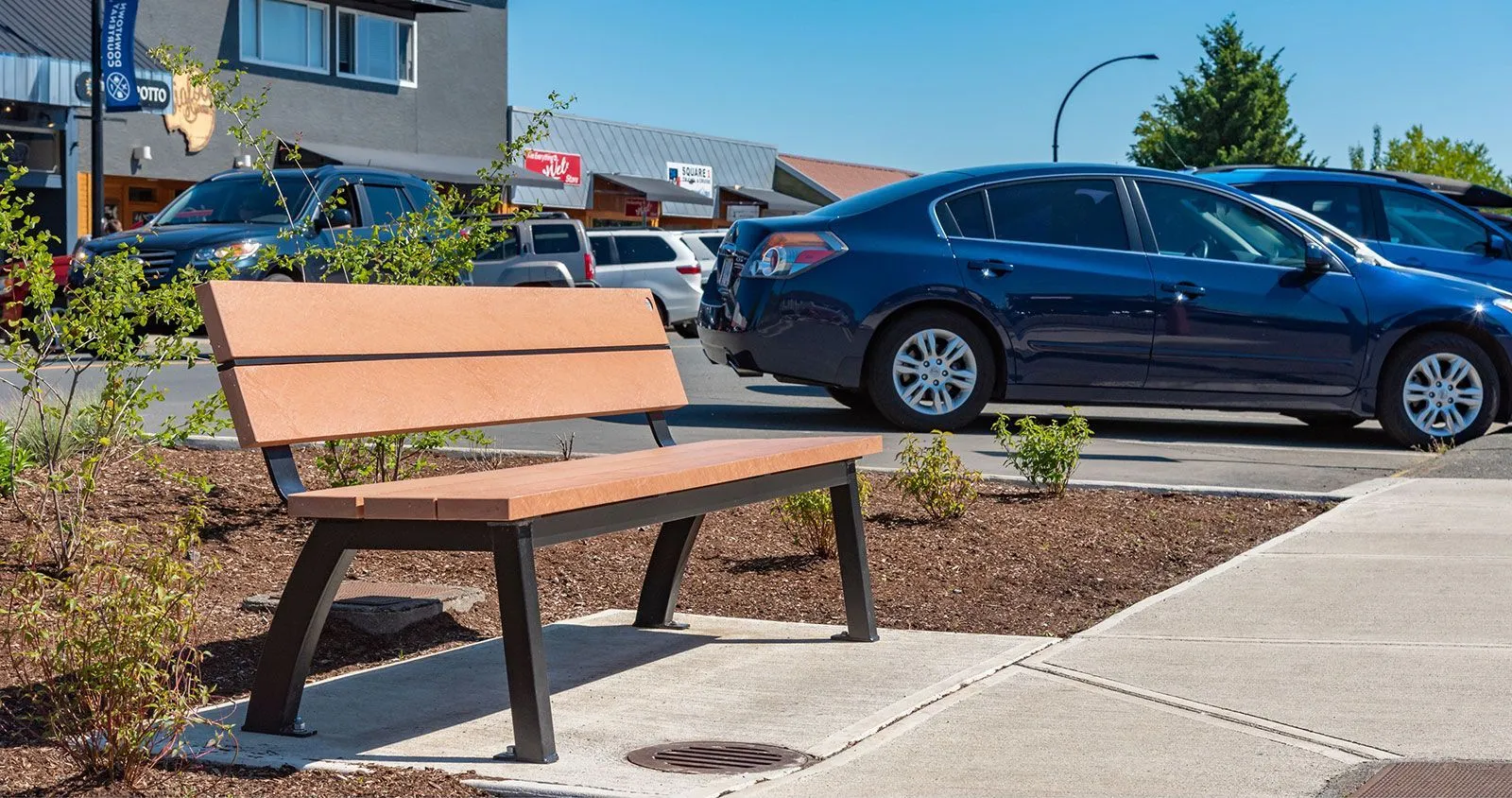 Aylesbury bench with recycled plastic lumber and powder-coated metal frame, providing comfortable seating in a commercial area. The bench offers a durable and stylish solution for outdoor public spaces.