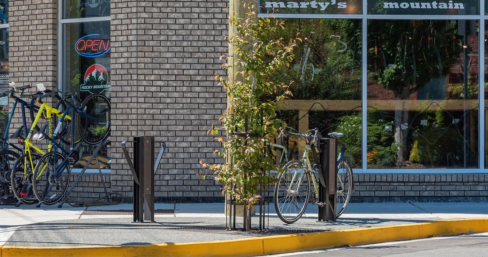 Durable bike racks provide secure parking outside a retail business. The racks are powder-coated in a dark color, complementing the urban streetscape.