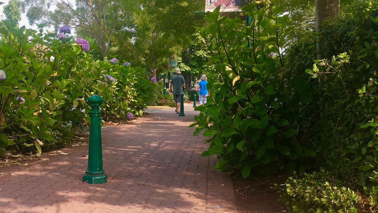 Classic bollards line a brick pathway in a garden setting. These bollards provide pedestrian guidance and safety in a lush, green environment.