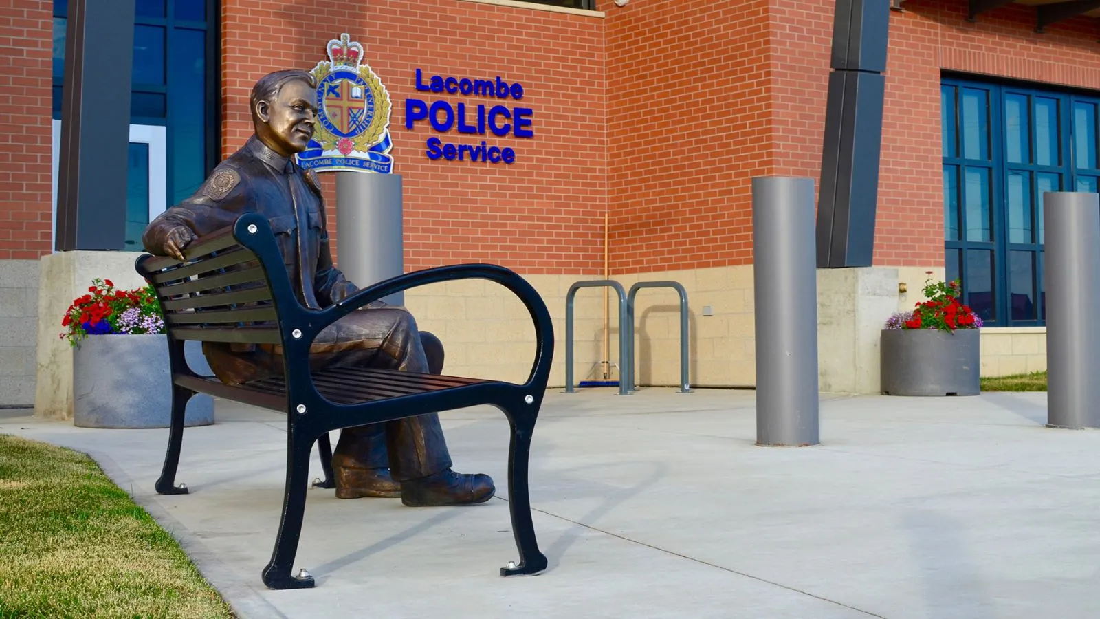 A Mountain Classic bench sits outside the Lacombe Police Service in Alberta, Canada. The bench provides a place for rest and contemplation near the building's entrance.
