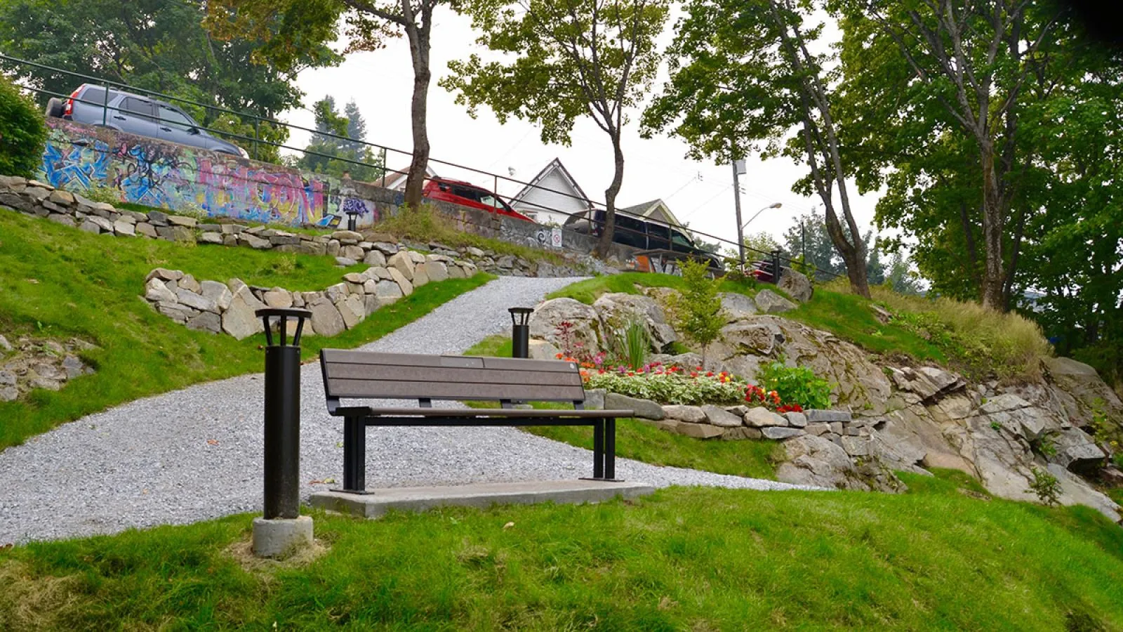 Larson bench seating along a gravel path in a landscaped park setting. The bench features recycled plastic lumber and a black powder-coated metal frame.