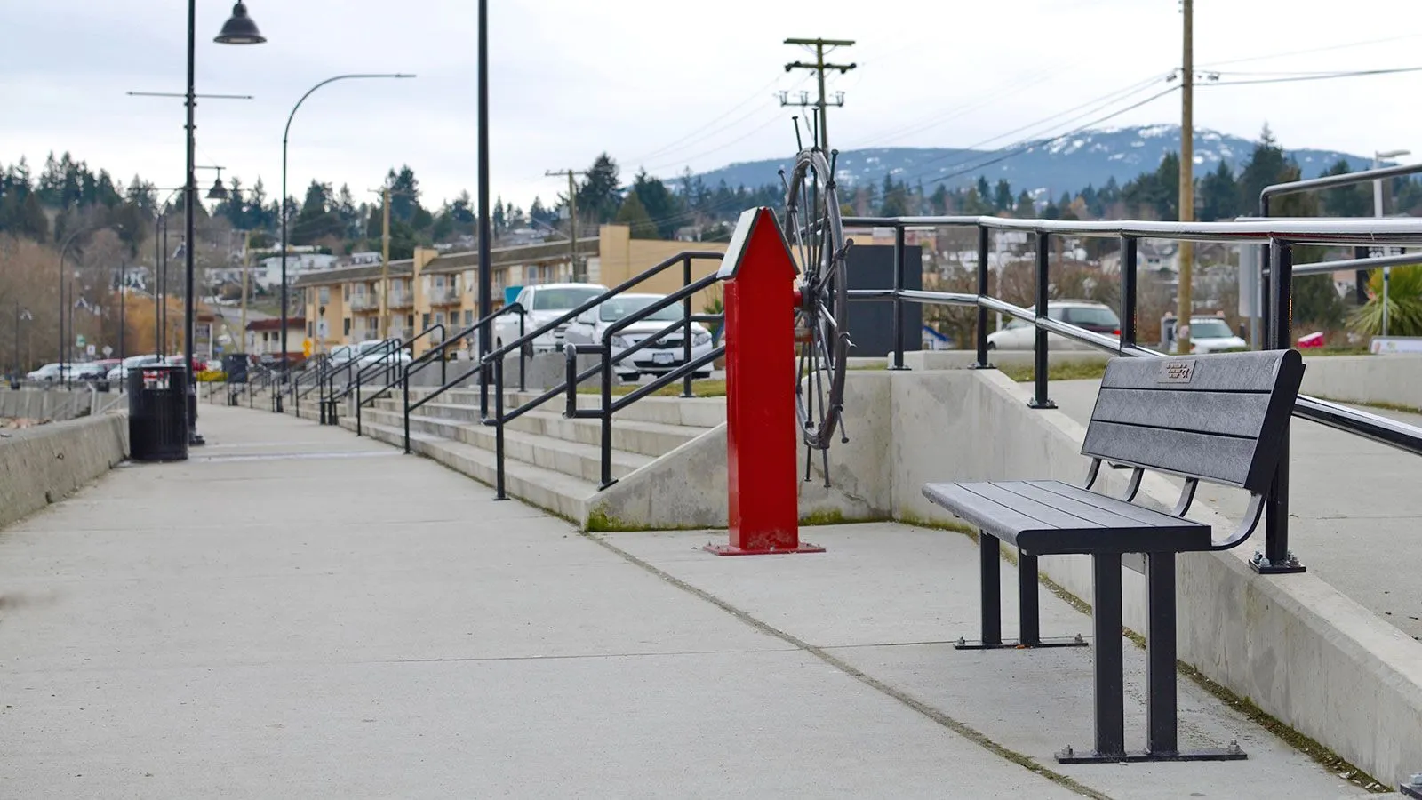 A Larson bench provides seating along a waterfront walkway. The bench features recycled plastic lumber and a powder-coated metal frame.