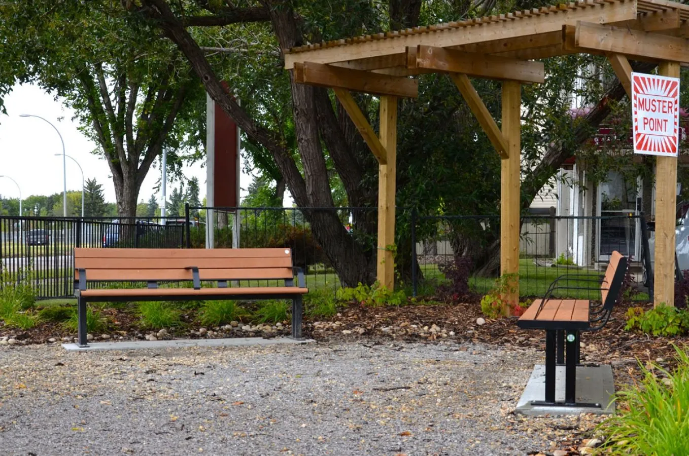 Larson benches with armrests provide seating in a landscaped area. The benches feature recycled plastic lumber and powder-coated metal frames.