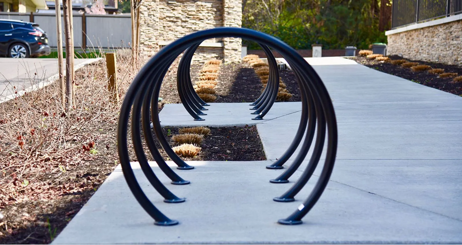 Loop Bike Racks provide secure and stylish bicycle parking along a paved pathway. The black powder-coated racks complement the surrounding landscaping.