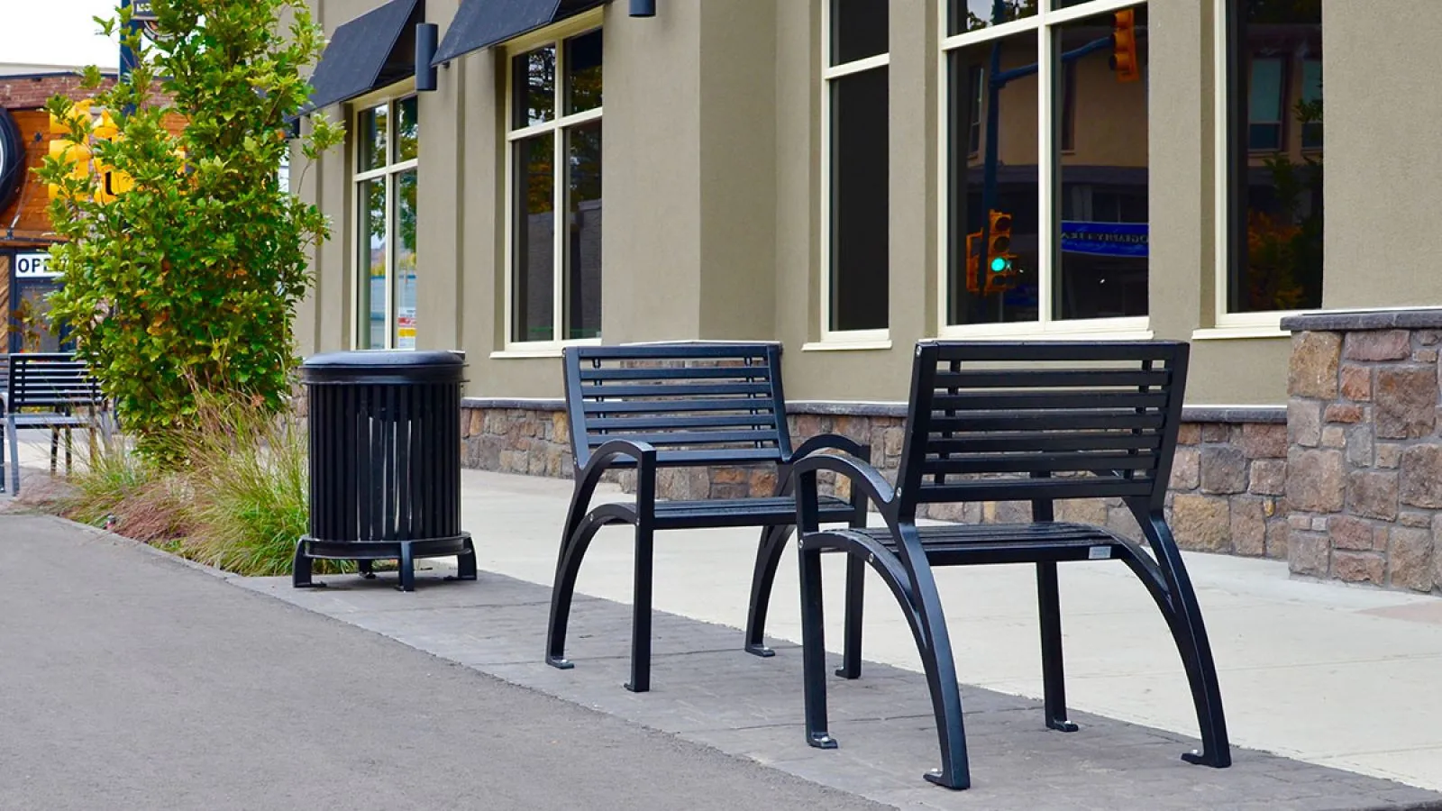 Outdoor seating area features a Beselt waste receptacle and Modena chairs with a black powder coat finish. These furnishings enhance the streetscape outside a commercial building in Vernon, British Columbia.