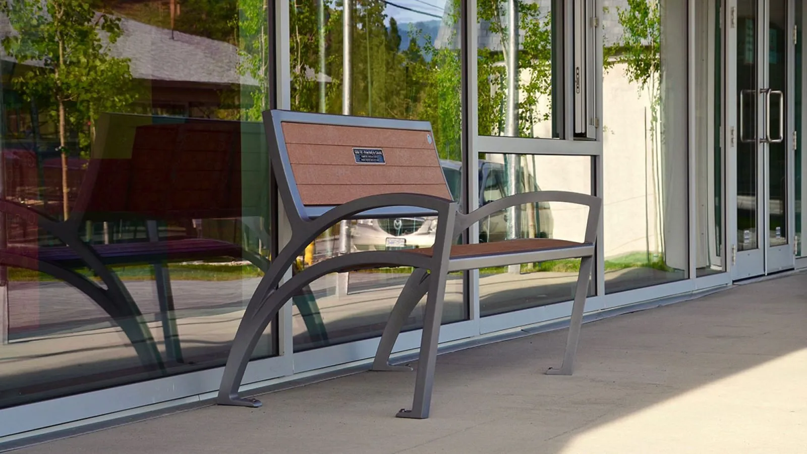 A Modena Wide Body Bench provides seating outside the Okanagan Regional Library in Summerland, British Columbia. The bench features recycled plastic lumber and a powder-coated metal frame.