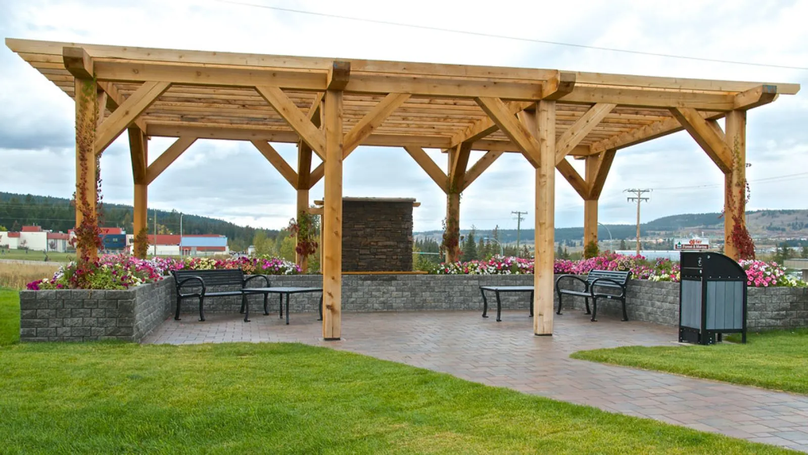 Outdoor benches and coffee tables create a welcoming rest area in a park setting. A waste receptacle is also present.