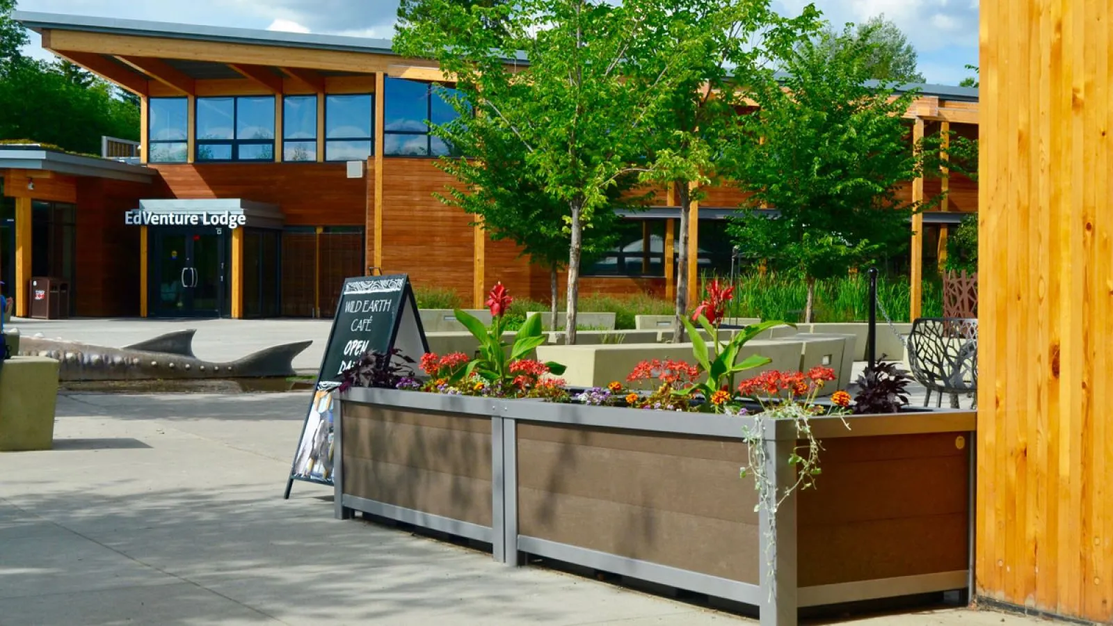 Rectangular self-watering planters add greenery to the entrance of the EdVenture Lodge at the Edmonton Valley Zoo. These planters feature recycled plastic lumber panels and a metal frame.