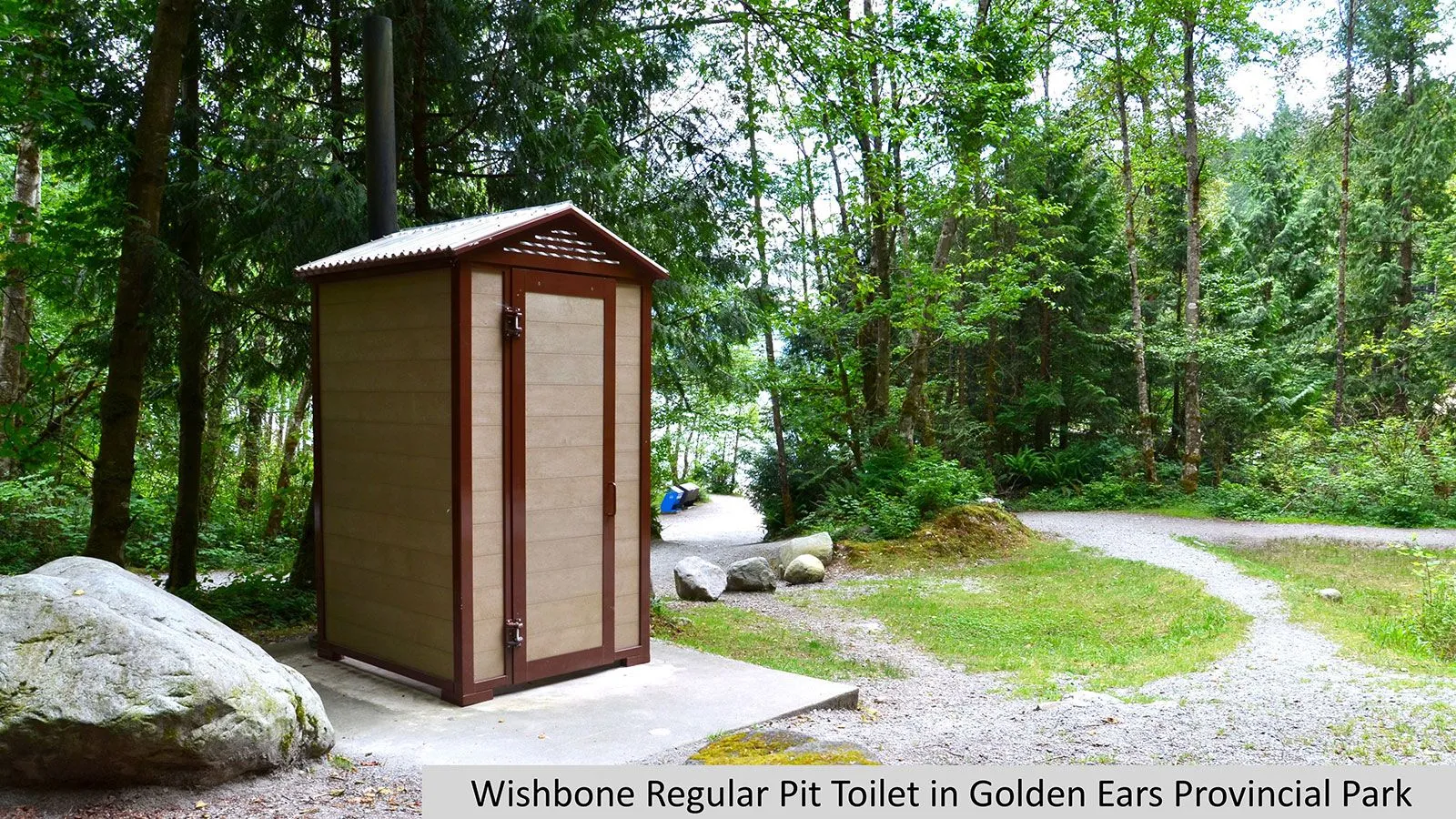 This pit toilet building is installed in a wooded area. The structure features recycled plastic lumber and a metal roof.