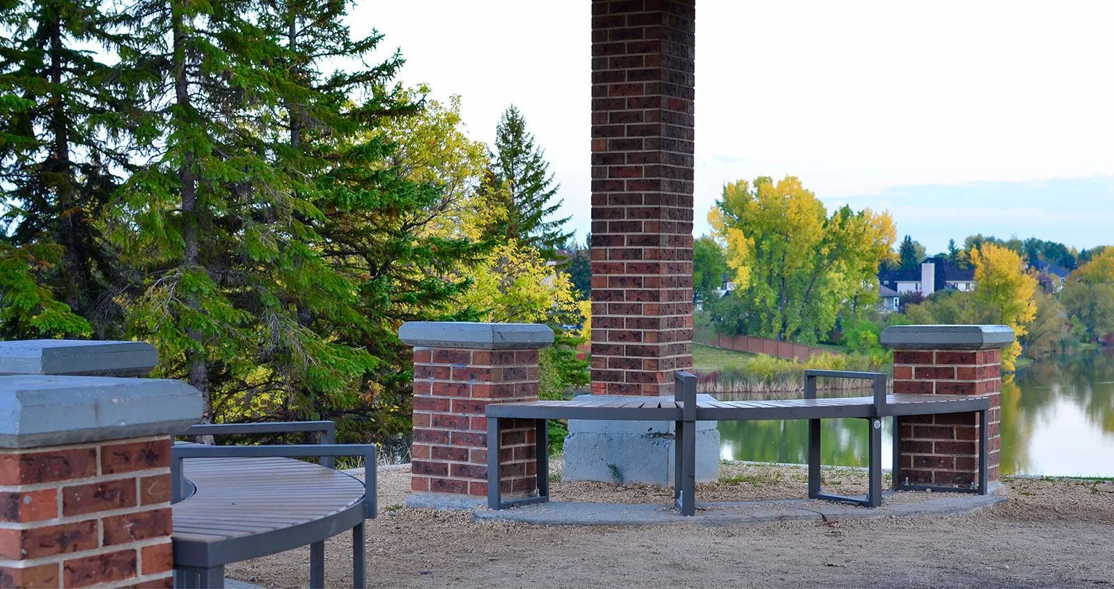 Curved benches provide seating in a park setting near a lake. The benches feature recycled plastic lumber and powder-coated metal frames.