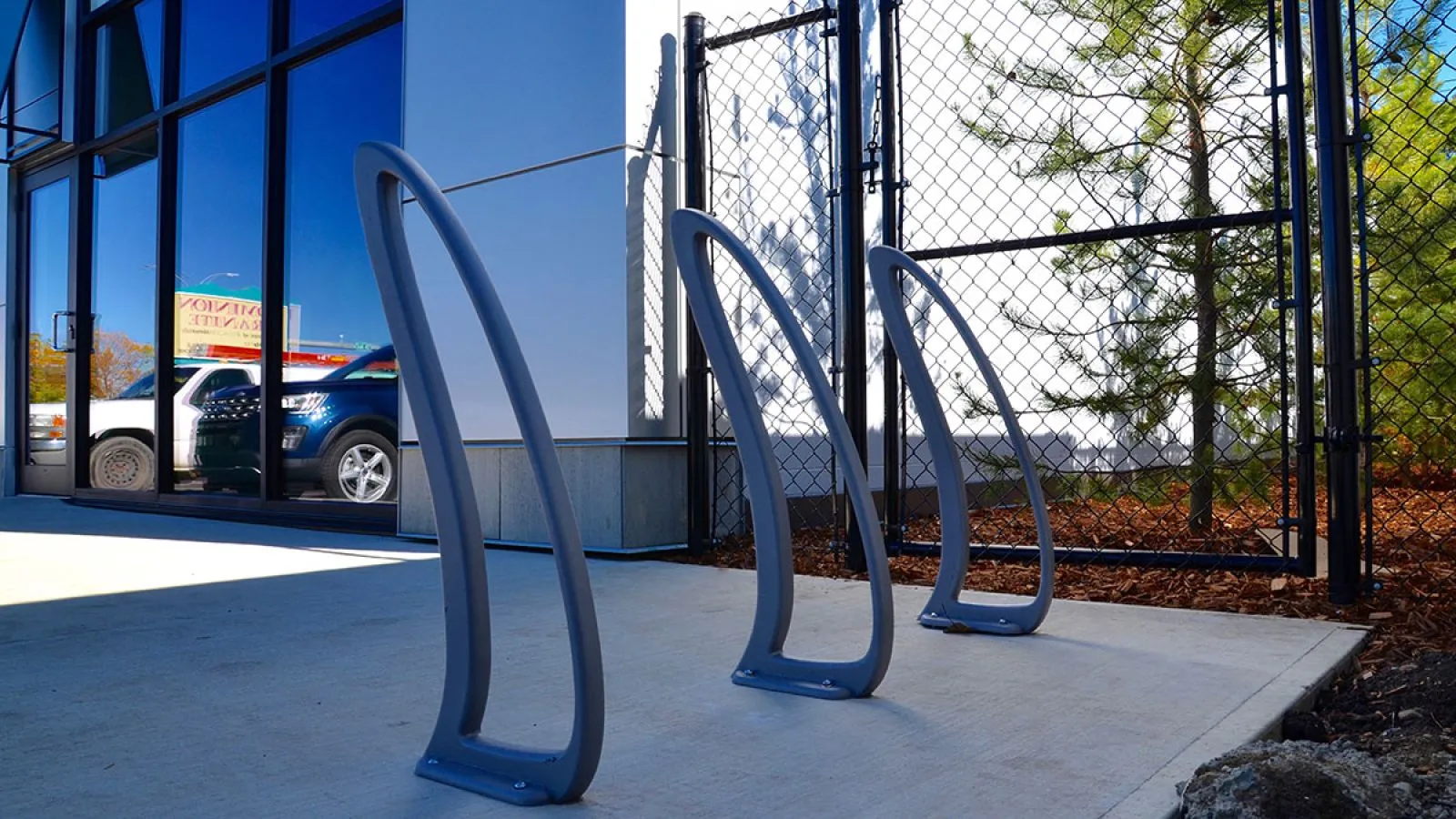 Three TENAJ bike racks provide secure parking outside a modern building. The bike racks feature a sleek, curved design and a durable powder-coated finish.