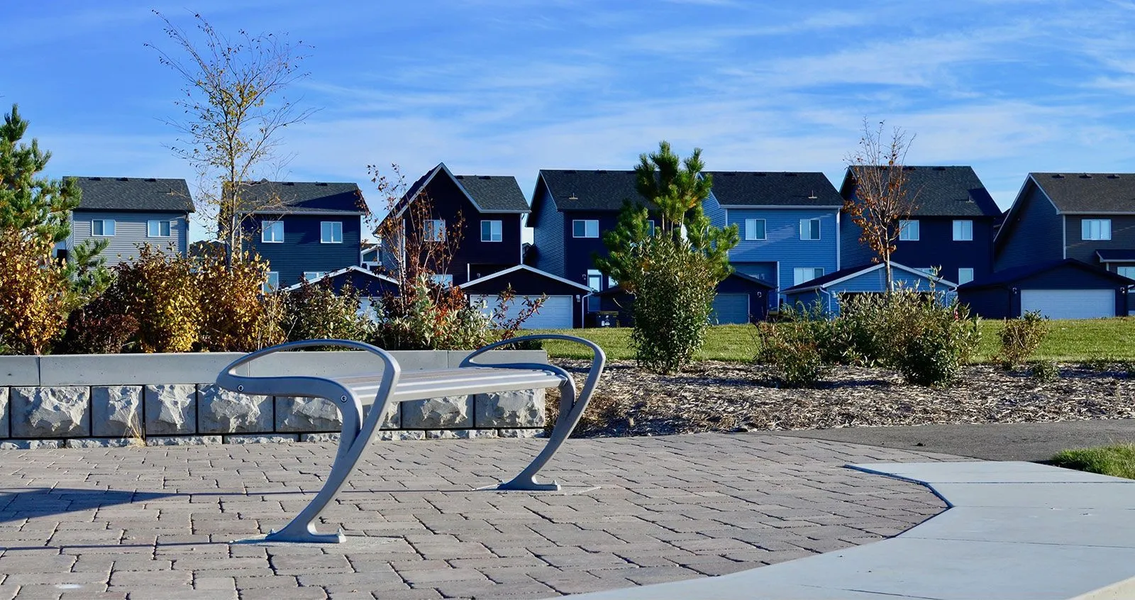 TENAJ straight bench provides seating in a residential area. The bench features a modern design with a curved frame and horizontal planks.