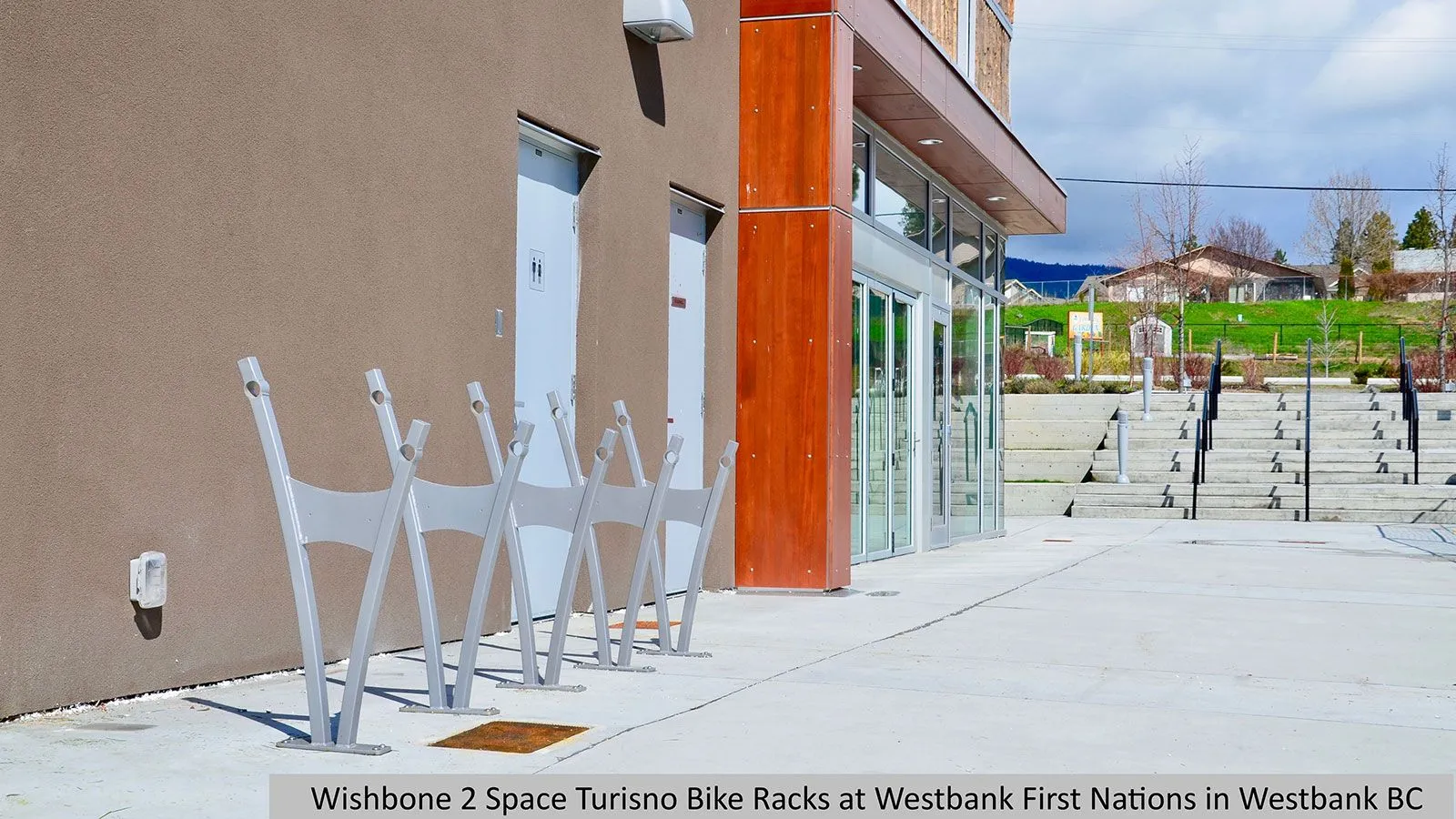 Two Turisno bike racks provide convenient parking outside a modern building. The racks are finished in silver, complementing the building's design.