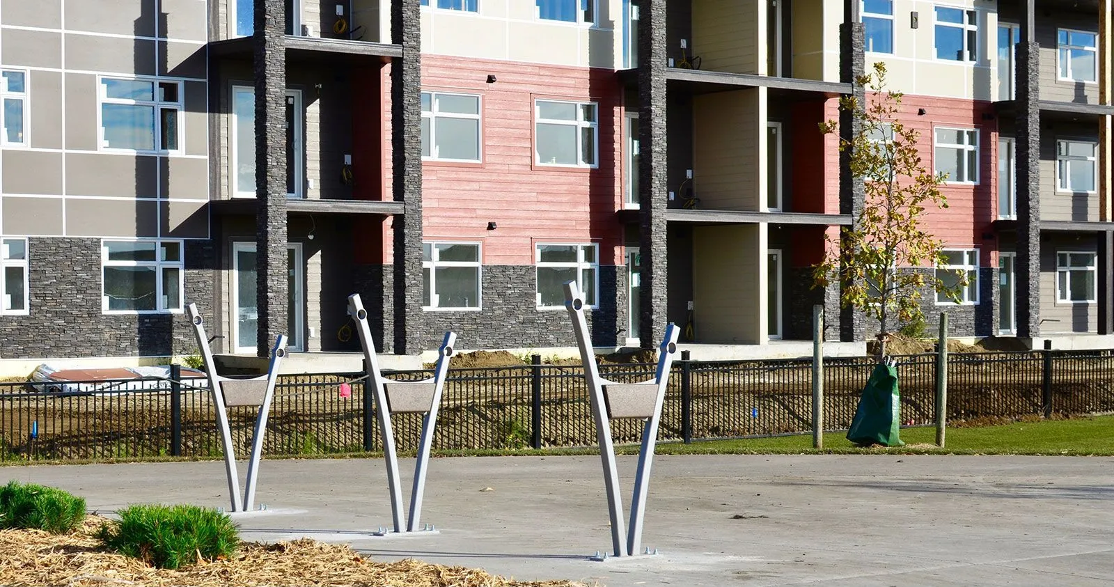 Three Turisno bike racks stand in front of a modern apartment building. These racks offer convenient and secure bicycle parking for residents.