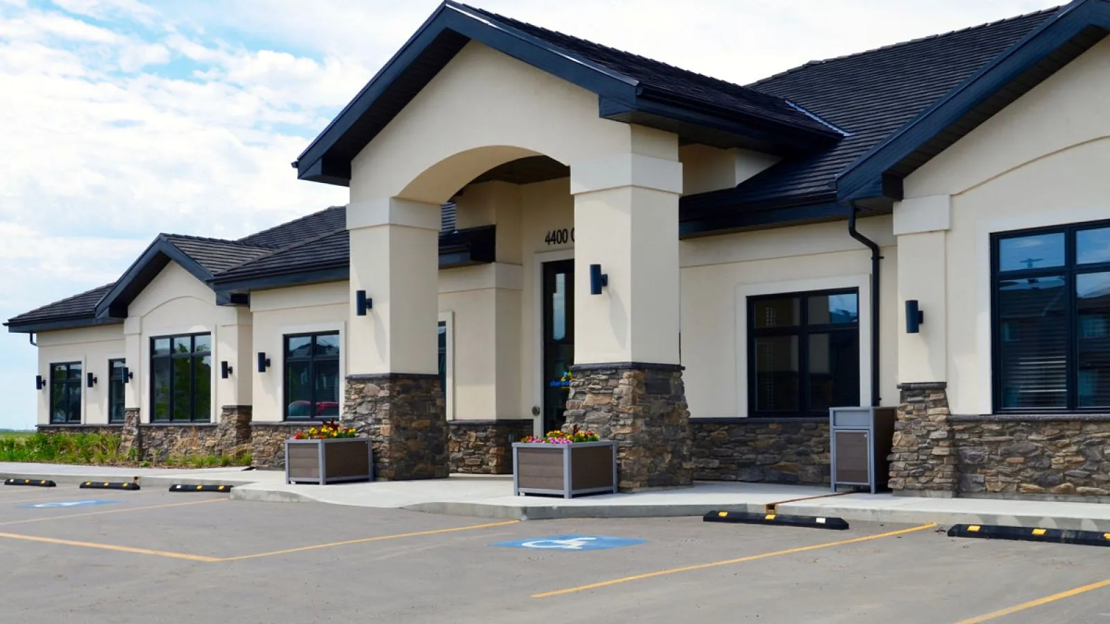 Urban Form square planters enhance the entrance of a building. These planters add greenery and visual appeal to the parking area.