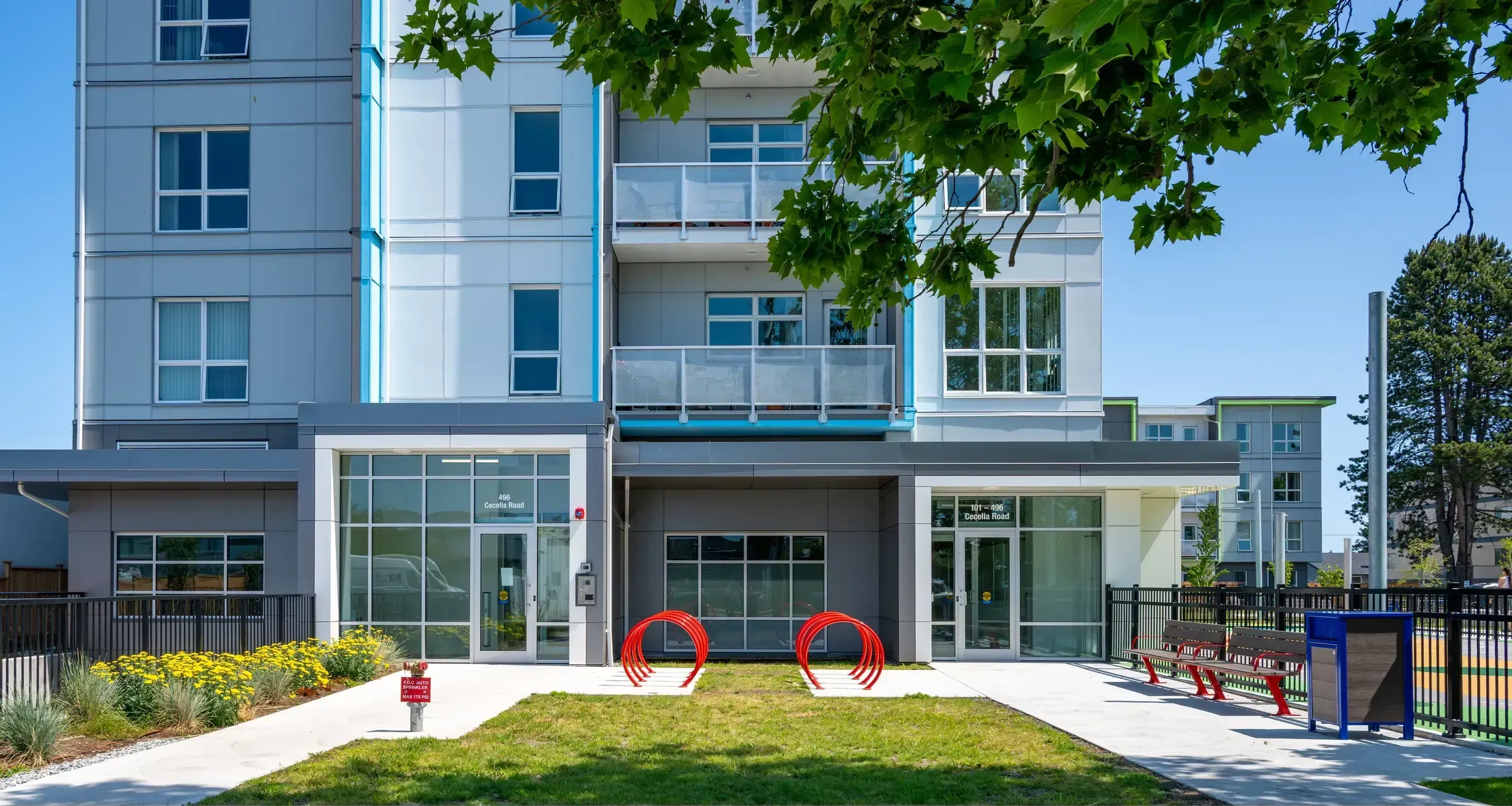 Outdoor space featuring a Bayview bench, Urban Form waste receptacle, and LOOP bike racks in front of a modern apartment building. The site furniture enhances the building's entrance and provides amenities for residents.