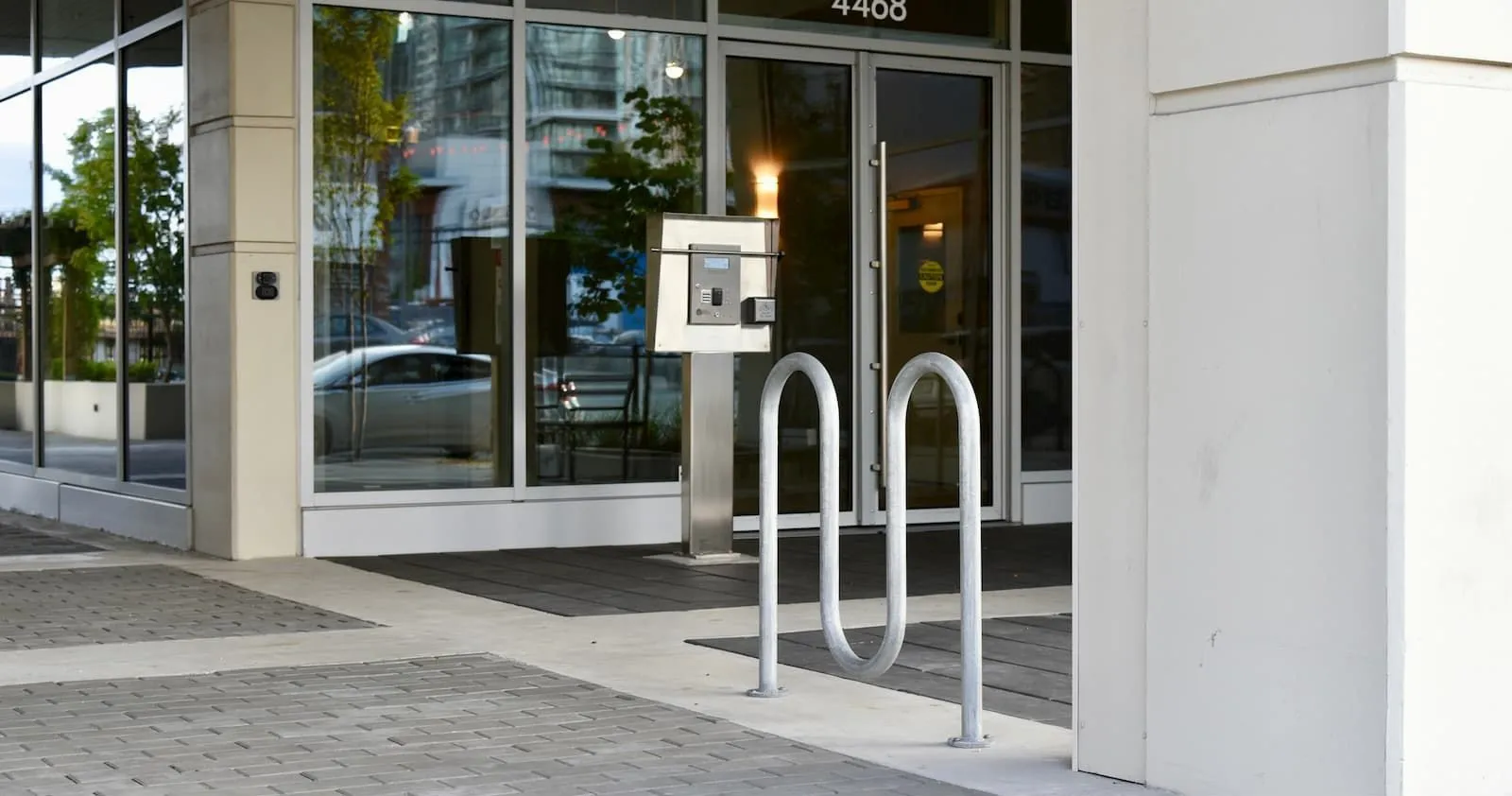 A Surf Bike Rack provides convenient parking outside a modern building. The rack is made of powder-coated metal.