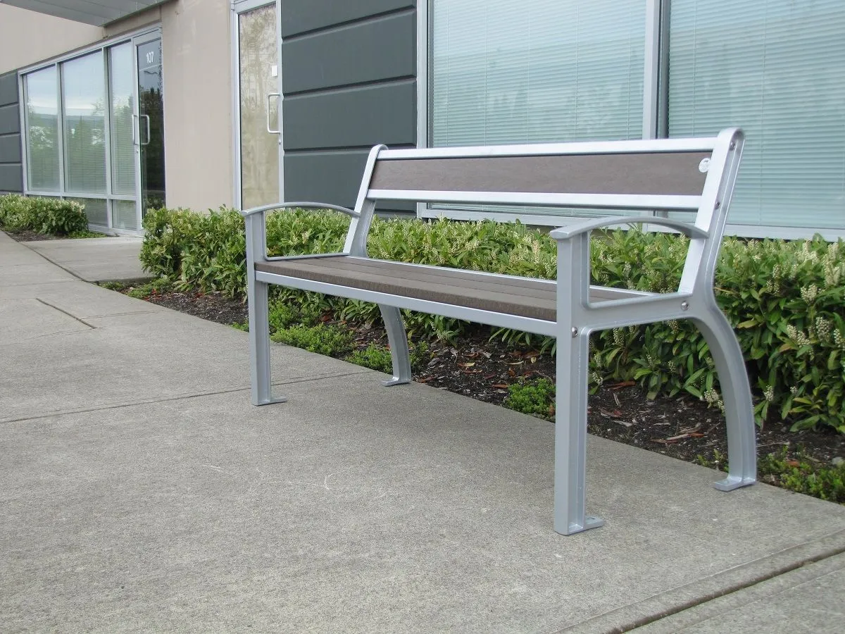 Beselt bench with silver powder-coated frame and recycled plastic lumber seat and back, installed on a concrete walkway outside a commercial building. Provides comfortable seating in an outdoor setting.