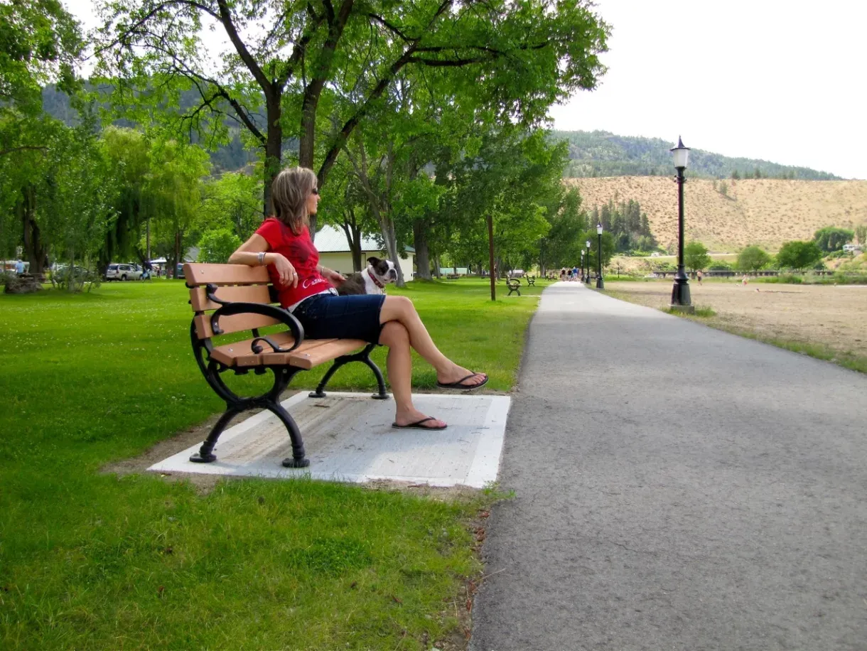 A Classic bench offers seating along a paved path in Okanagan Falls, British Columbia. The bench features recycled plastic lumber and a durable metal frame.
