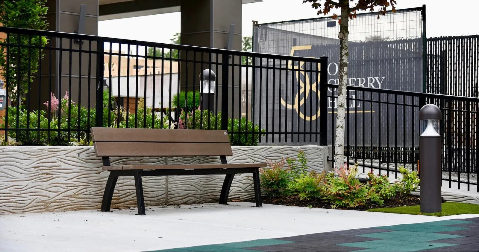 Aylesbury bench with recycled plastic lumber and black powder-coated frame sits in a landscaped area. The bench provides seating near a building under construction.
