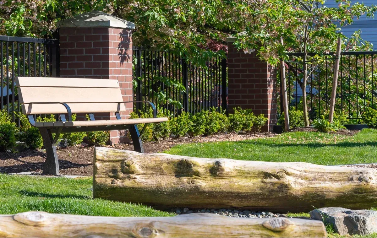 A Parker bench provides seating in a landscaped park setting. The bench features recycled plastic lumber and a powder-coated metal frame.