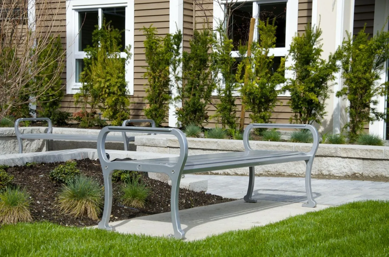All-metal Mountain Classic straight benches provide seating in a landscaped area. The benches feature a simple, durable design suitable for outdoor public spaces.