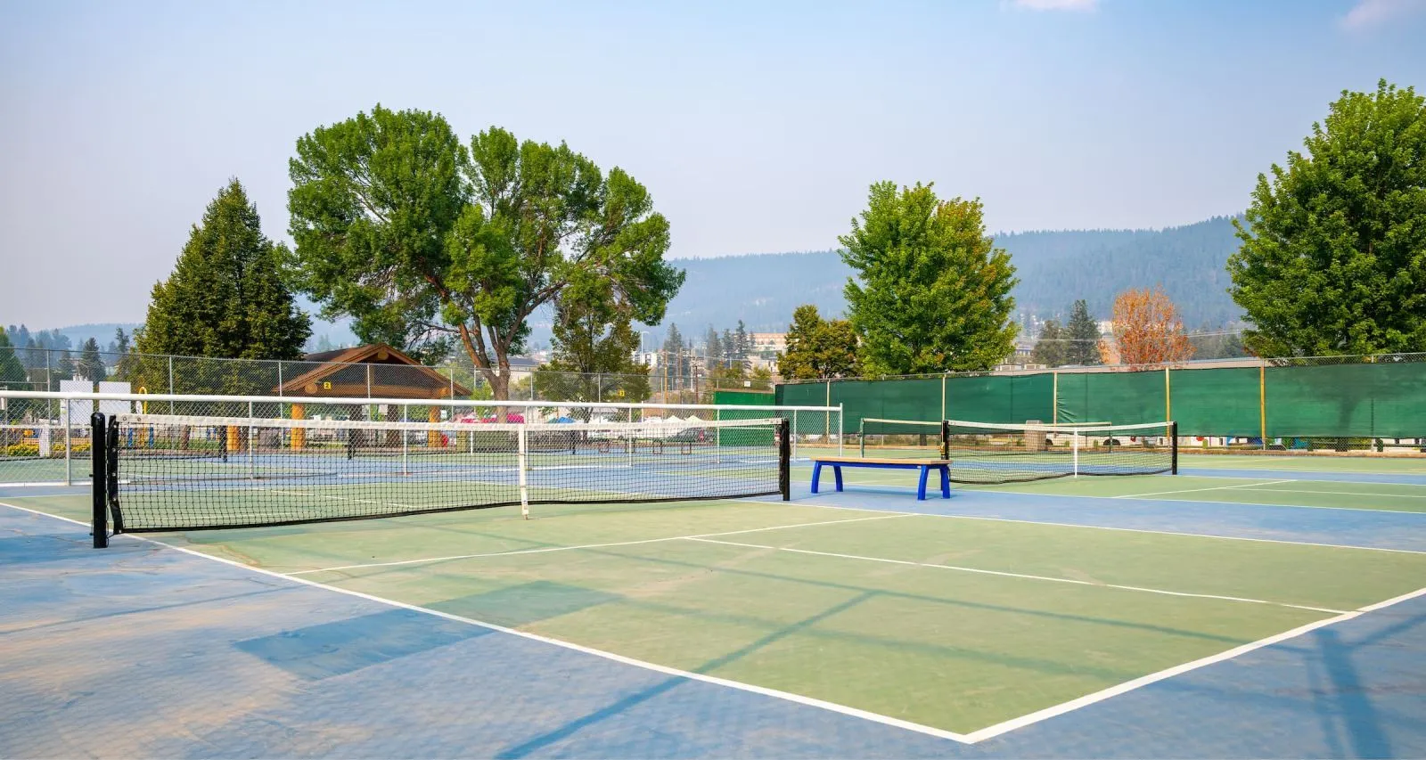 Backless bench in a blue powder coat sits on the edge of a pickleball court. The courts are located at Kiwanis Park in Williams Lake, British Columbia.