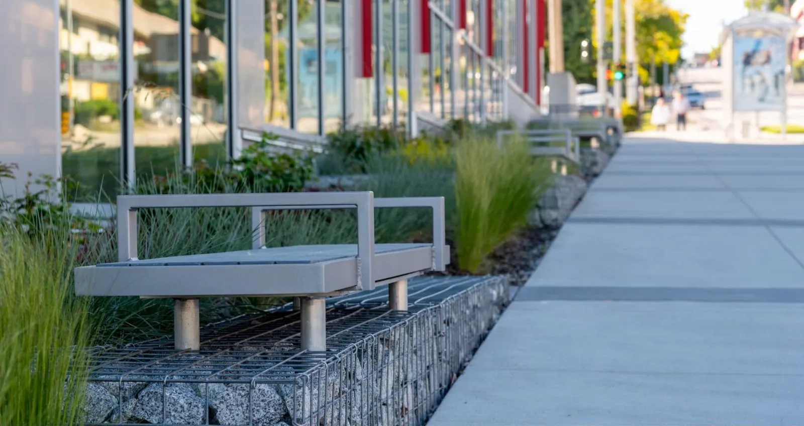 Backless Skyline benches provide seating along a sidewalk in front of a building. The benches feature a metal frame and recycled plastic lumber.