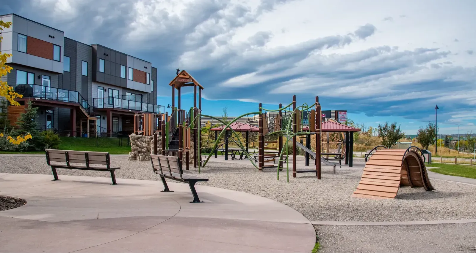 Bayside benches provide seating at the Trinity Hills Playground in Calgary, Alberta. The benches offer a place to rest near the play equipment and modern townhouses.
