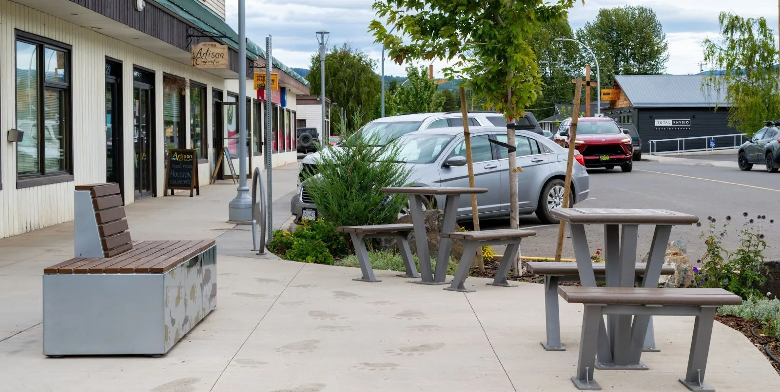 Outdoor seating area featuring a Bayview bench and table set on a paved sidewalk. The site furniture provides a place to rest and gather in the town of Houston, British Columbia.