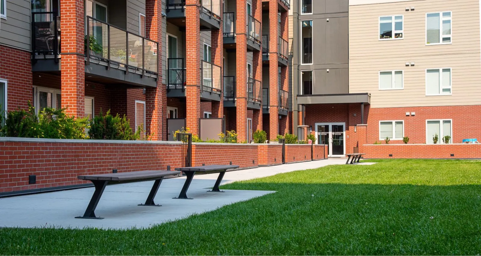 Bayview backless benches provide seating in a courtyard at Thompson Rivers University. The benches feature a simple design with dark lumber and black metal frames.