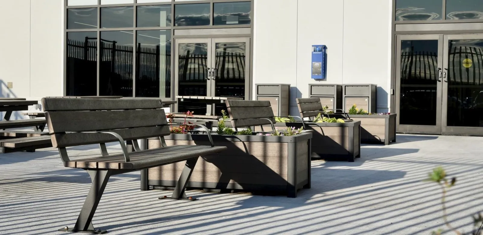 Bayview benches are paired with Urban Form rectangular planters and waste receptacles in an outdoor setting. The benches feature recycled plastic lumber and powder-coated metal frames.
