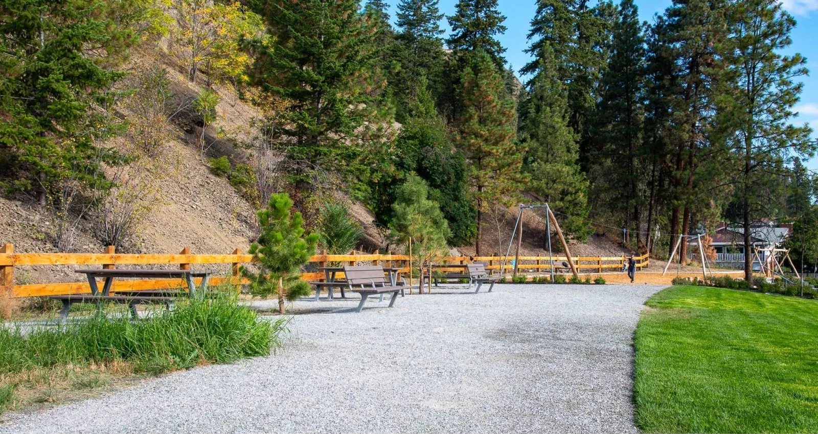 Bayview picnic tables and benches provide seating in Ballou Park. The park features a gravel path, grassy areas, and a wooden fence.