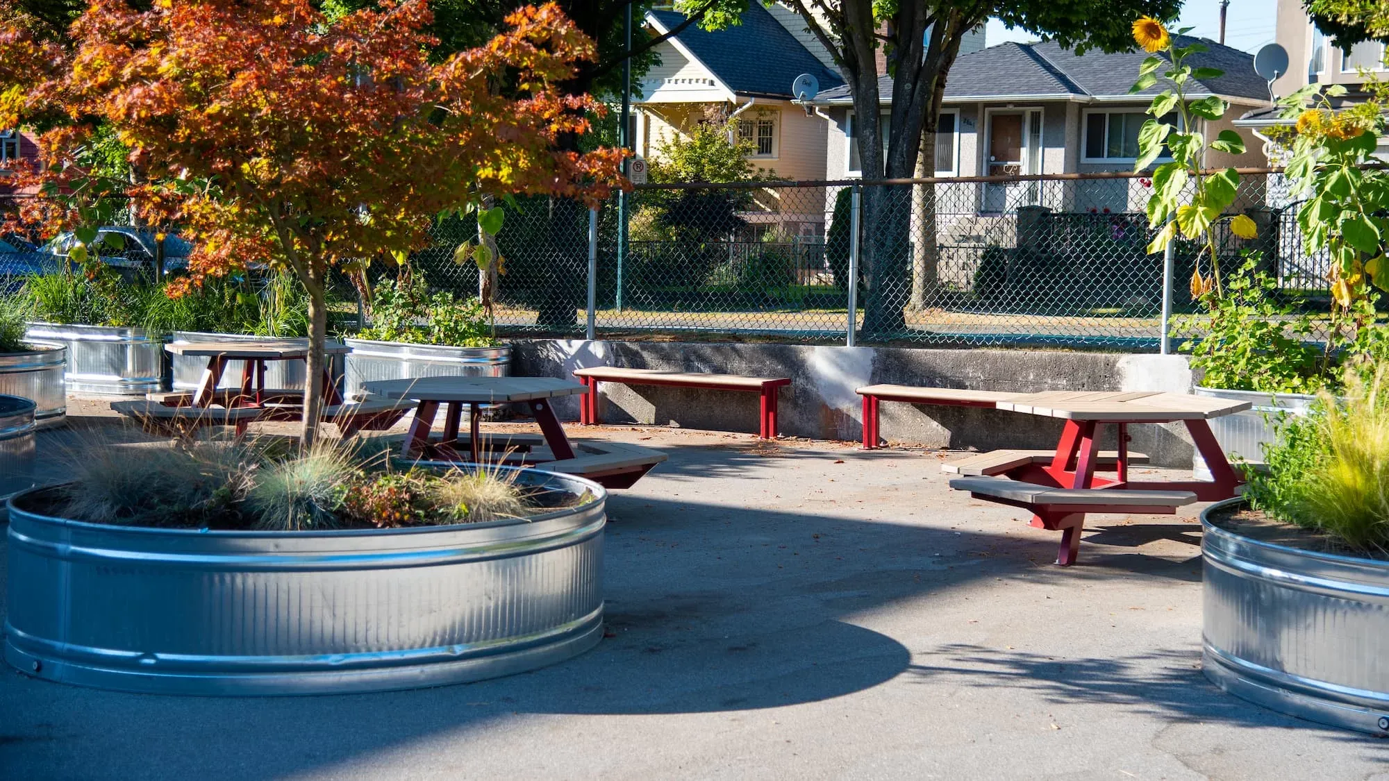 Bayview Hexagonal Picnic Tables and Larson Backless Benches create a welcoming outdoor space at Hastings Elementary School in Vancouver, BC. Galvanized steel planters add greenery to the paved area.