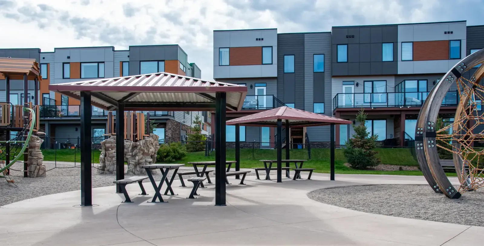 Bayview picnic tables provide shaded seating at Trinity Hills Playground in Calgary, Alberta. The tables feature a black powder-coated frame and natural-toned recycled plastic lumber.
