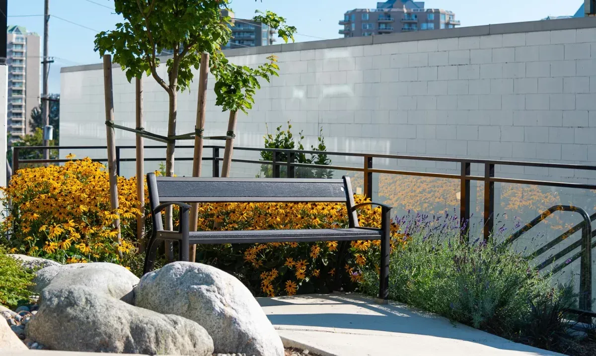 A Beselt bench is nestled amongst colorful flowers and greenery. This site furniture provides a comfortable resting spot in a landscaped outdoor area.