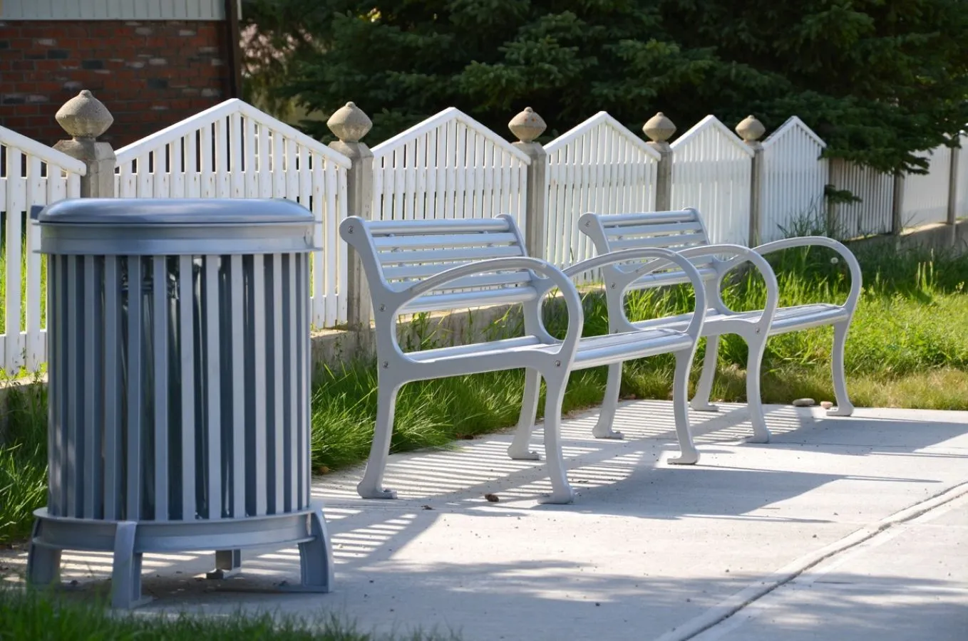 A Beselt round waste receptacle and Mountain Classic benches provide seating and waste disposal in an outdoor setting. The benches and bin are powder-coated in a light grey finish.