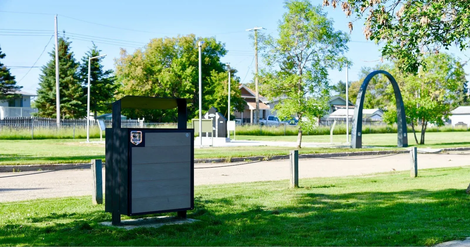 City Scape waste receptacle in a park setting. The bin features horizontal recycled plastic lumber slats and a black powder-coated metal frame.