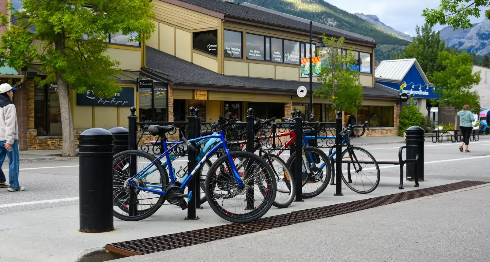 Bicycles are parked at a Classic 2 Space Bike Rack in a commercial area. The bollard-style rack provides secure parking along the sidewalk.