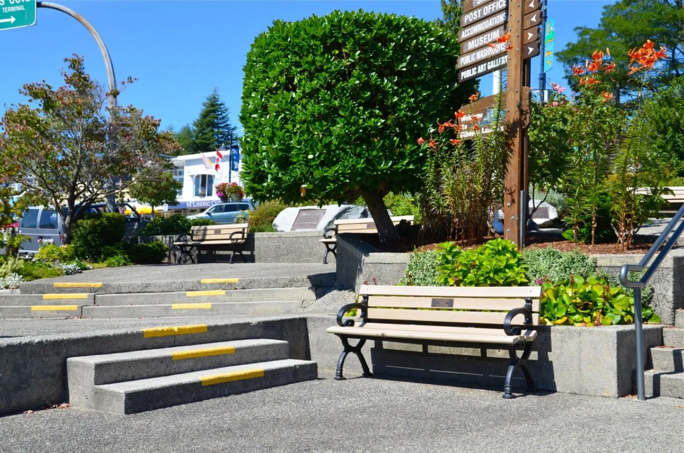 Classic benches provide seating in a landscaped public space. The benches feature recycled plastic lumber and powder-coated metal frames.