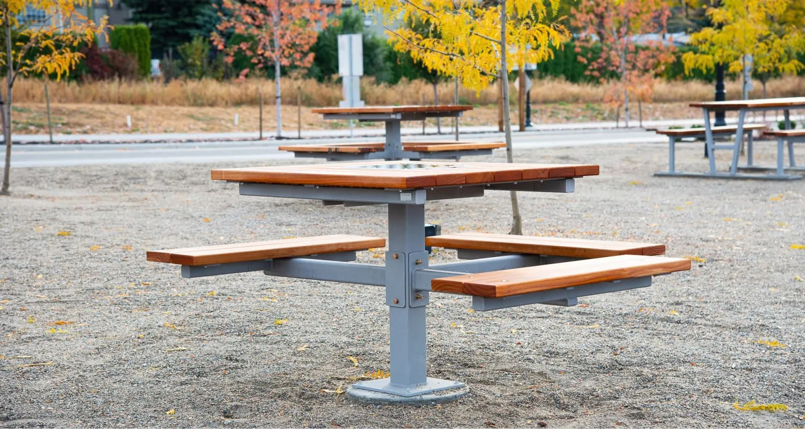 This wheelchair-accessible picnic table features a single pedestal design with a square tabletop and attached seating. The table is made with durable materials and is perfect for outdoor use in parks and other public spaces.