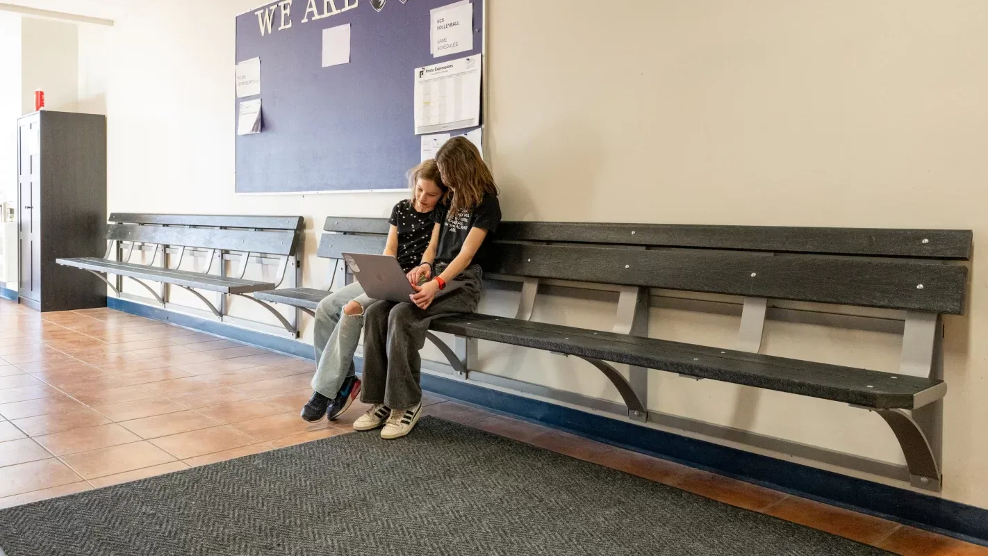 Wall-mounted bench seating provides a place for students to relax and study in a school hallway. The benches feature recycled plastic lumber and a durable metal frame.