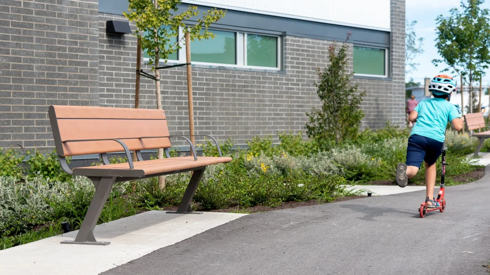 Bayview Plus bench with recycled plastic lumber and powder-coated metal frame provides comfortable seating along a pathway. This site furniture enhances public spaces.