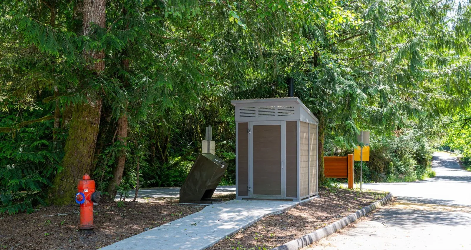 Forest Series regular outhouse building in a wooded park setting. The structure features recycled plastic lumber and a metal roof.