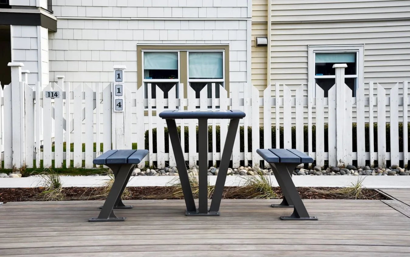 This bistro table and bench combo provides a simple and functional outdoor seating solution. The set features a table and two benches with a gray finish, set on a wooden deck.