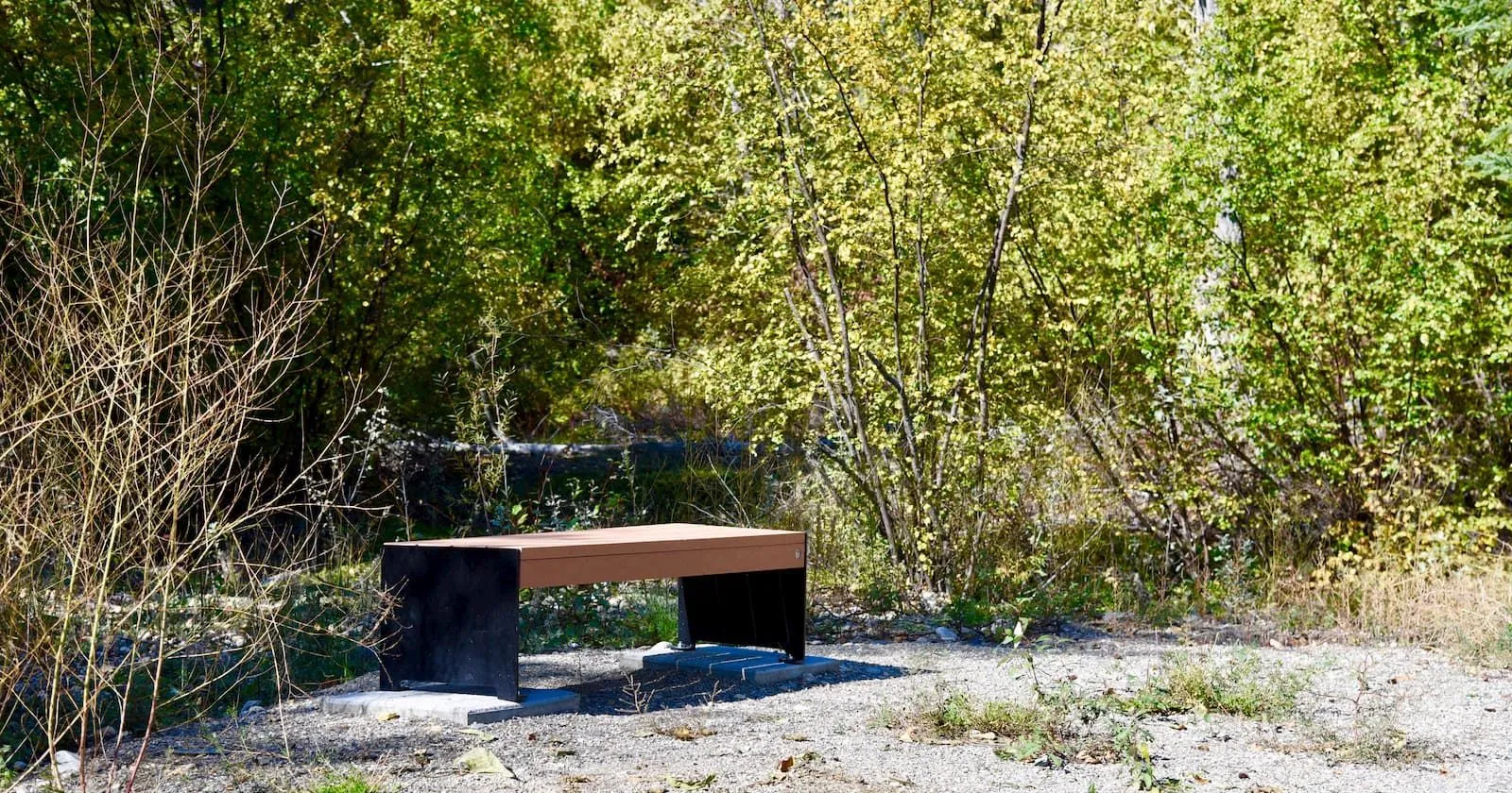 A Hutch Backless Bench provides seating in a natural setting. The bench features recycled plastic lumber and a powder-coated metal frame.